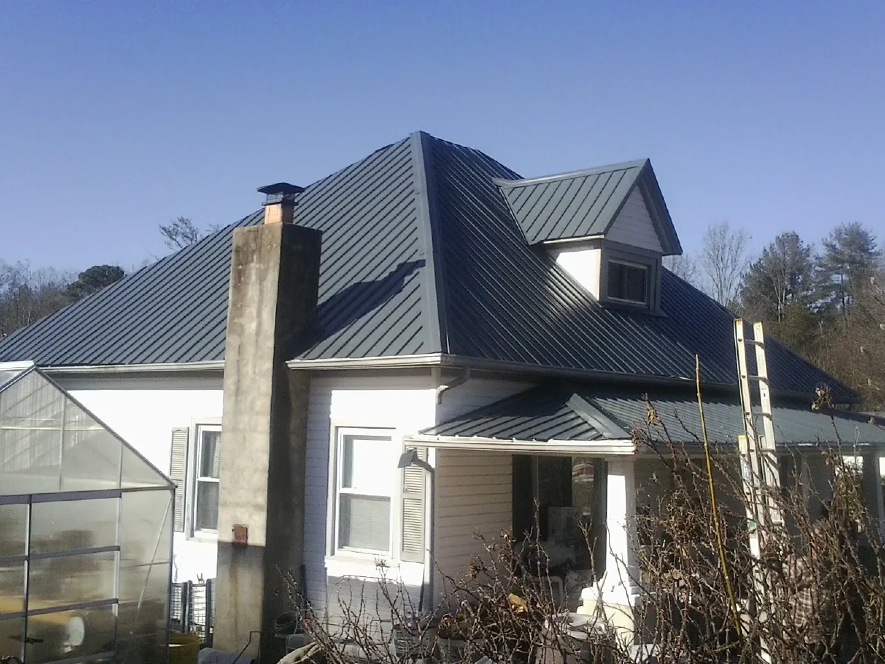 Dark blue standing seam metal roof on a white farmhouse with dormer — Slate & Tile Roof Repair by Roofing Brothers in Stanton